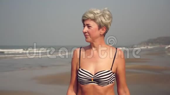 穿着泳衣的成熟迷人的女人正沿着海滩散步海上美丽的祖母视频的预览图