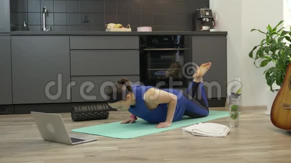 坚强自信的女孩在家厨房做俯卧撑练习穿着运动服的漂亮健身女士在网上锻炼视频的预览图