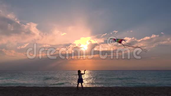 孩子在海滨海滩玩耍孩子在海上日落时放风筝快乐的小女孩在海岸线上视频的预览图