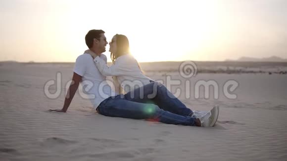 年轻的男人和女人坐在沙漠中美丽的夫妇女孩和男人沙丘景观背景轻微的黄昏浪漫浪漫视频的预览图