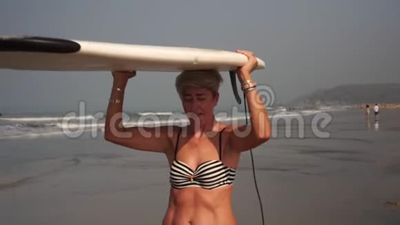 成熟的成年女人在海滩上拿着冲浪板奶奶是个冲浪者视频的预览图