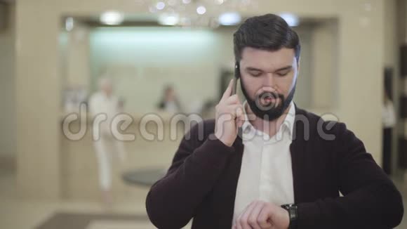 一个英俊的白人黑发男人留着胡子挂着电话在模糊的接收背景下对着镜头微笑视频的预览图