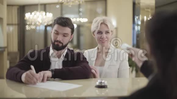 积极的白人男子签署文件的肖像他的配偶从接待员拿走房间钥匙卡结婚快乐视频的预览图