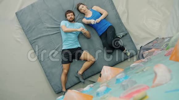 男人和女人谈论室内攀岩的俯视图躺在垫子上指向墙壁视频的预览图