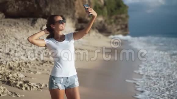 美丽的年轻女子在沙滩上的智能手机上自拍视频的预览图