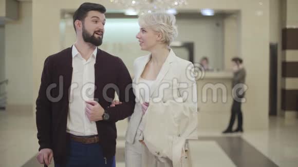 美丽的白种人年轻夫妇在豪华的酒店大厅里交谈和看相机自信的有钱男女视频的预览图
