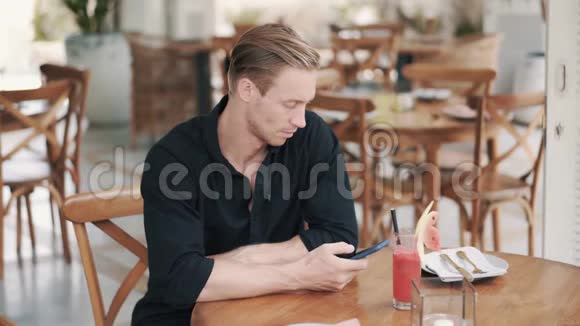 穿衬衫的帅哥坐在咖啡馆里喝果汁用电话视频的预览图