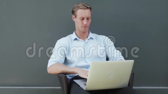 男人在笔记本电脑上工作看着屏幕微笑着背景上有灰色的墙壁视频的预览图