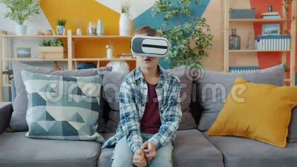 享受虚拟现实眼镜的孩子坐在家里的沙发上做着放松的手势视频的预览图