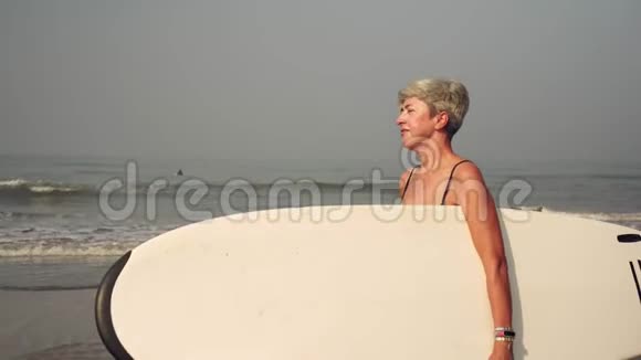 奶奶沙滩上成熟的女人拿着冲浪板视频的预览图