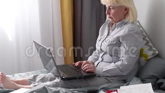 成年女性穿着条纹衬衫和家用裤子坐在家里卧室里的笔记本电脑上工作家工作理念工作视频的预览图