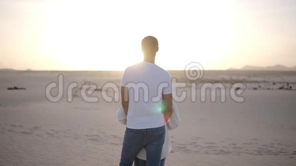 一对年轻夫妇站着拥抱着男人从后面抱着她的女人在干燥的沙漠里看着风景视频的预览图