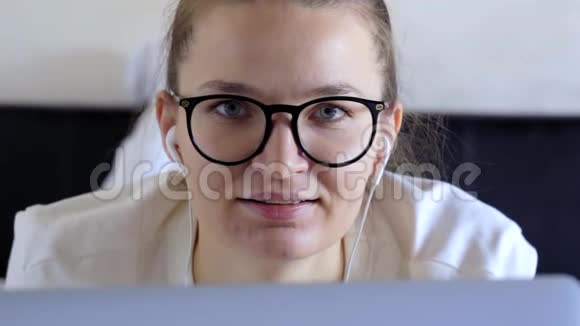 快乐的年轻女人戴牙套在家里的办公室看着相机戴眼镜和耳机的女学生正面肖像视频的预览图