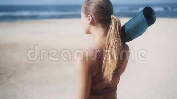 后视图穿着运动服带着体操垫的年轻女子去海滩视频的预览图