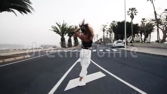 兴奋的年轻时尚女人穿着白色裤子摆姿势在路上跳舞背景是棕榈树和其他视频的预览图