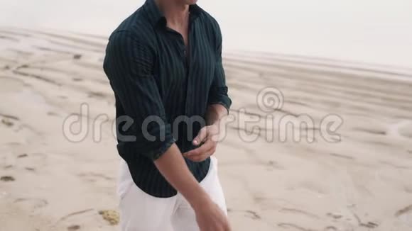 孤独的男人穿着黑色衬衫沿着沙滩散步视频的预览图