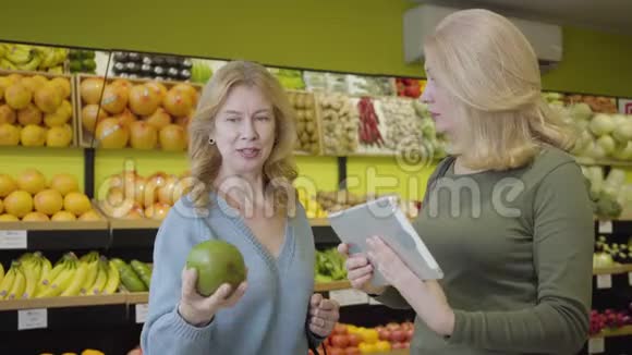 成年白种人女性使用平板电脑检查水果来源积极的家庭主妇在杂货店买柚子生活方式视频的预览图