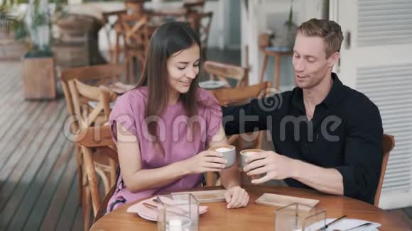 年轻夫妇在咖啡馆喝咖啡男人和女孩谈笑风生视频的预览图