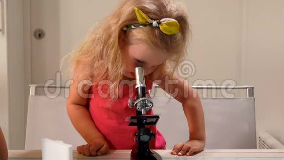 可爱的金发女郎穿着粉红色的衣服正透过显微镜看镜头视频的预览图