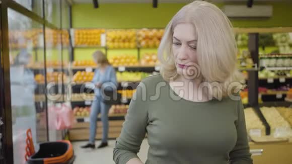 严肃的白人女性在杂货店冰箱里挑选产品的特写镜头成人集中女士视频的预览图