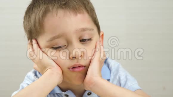 儿童肖像男孩坐在桌边双手捧着脸流露出悲伤体贴的情绪视频的预览图