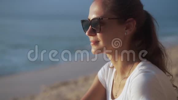 美丽的年轻女子戴着太阳镜在海边看天空和日落视频的预览图