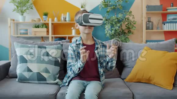 男孩尝试虚拟现实眼镜环顾四周打手势坐在公寓的沙发上视频的预览图