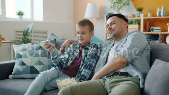 中年男子父亲看电视儿子开心地在家里的沙发上放松视频的预览图