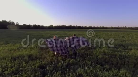 日落时分一个女孩和一个盖着格子布的家伙正穿过绿茵场视频的预览图