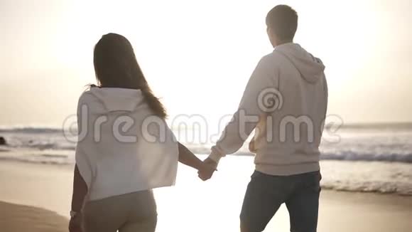 背面的景色年轻夫妇相爱手牵手走在海滩上的休闲服装海底日落视频的预览图
