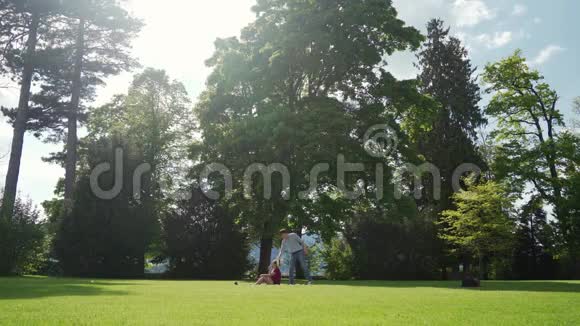 在美丽的绿色公园野餐时有趣的家伙在女孩身边挥舞着帽子阳光明媚视频的预览图