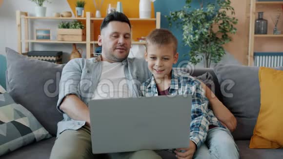 成年男子和小孩用手提电脑打字看屏幕在家大笑视频的预览图