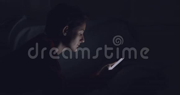 有手机的女人躺在床上晚上浏览视频的预览图