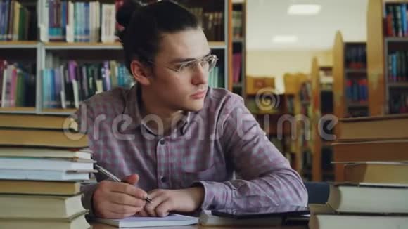 年轻英俊的少年戴着眼镜坐在大学图书馆的桌子上思考着复印本中的计算视频的预览图