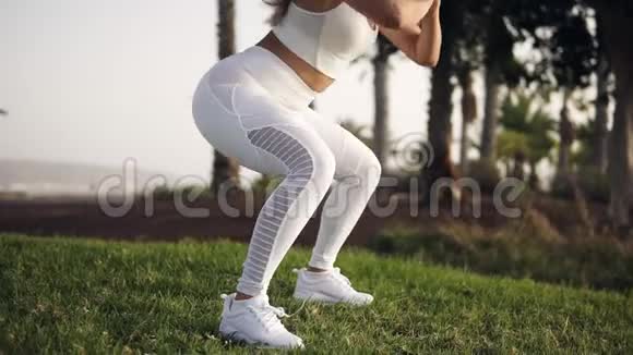 年轻漂亮的女孩穿着白色紧身裤白色运动鞋在背景的棕榈树上做运动视频的预览图