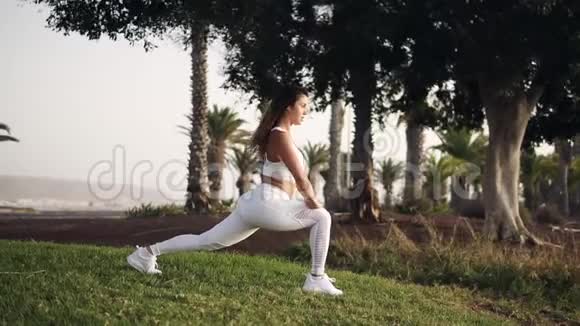 穿白色运动服的运动女性做瑜伽姿势或户外伸展运动运动女孩在公园里伸展健身视频的预览图