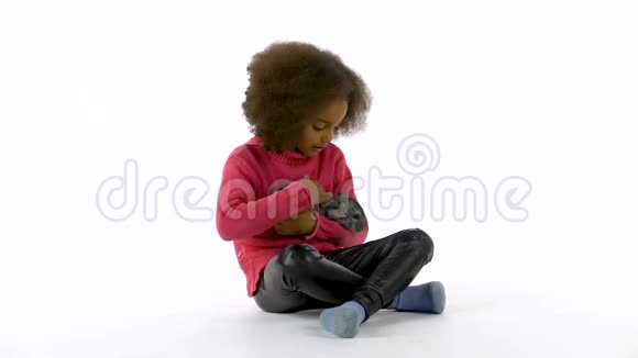 小非洲卷曲的女孩抱着灰色的下巴抚摸着白色的背景慢动作视频的预览图