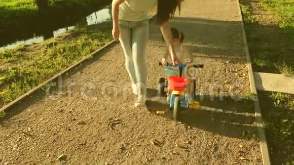 一个小孩子学会骑自行车由他的母亲妈妈教女儿在公园里骑自行车妈妈在玩视频的预览图