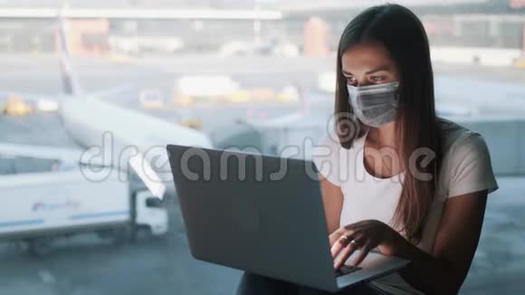 戴防护口罩的女孩在机场工作时使用笔记本电脑视频的预览图