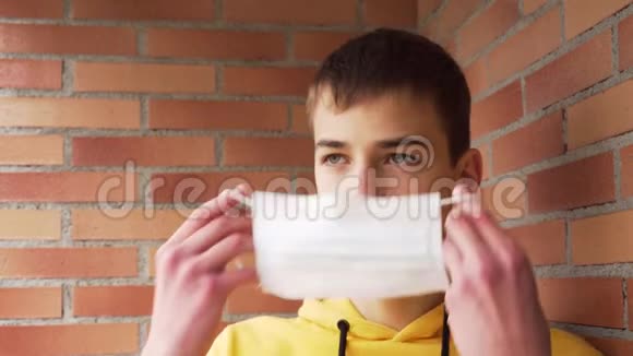 年轻人正对着砖墙戴上一个保护性医疗面具视频的预览图