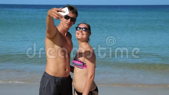 微笑幸福的情侣在蔚蓝的海洋附近阳光明媚的海滩上自拍视频的预览图