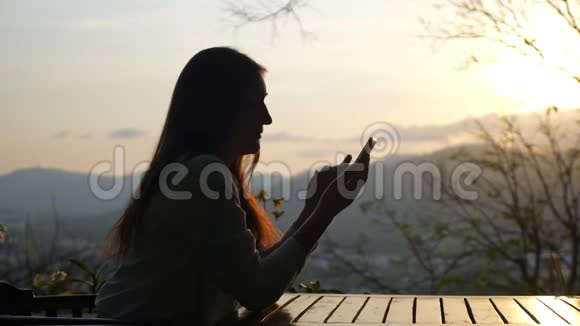 一个年轻的女人坐在户外咖啡馆的桌子旁拿着电话视频的预览图
