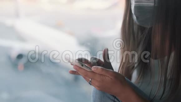 戴防护面罩的女士使用智能手机在机场发送信息视频的预览图