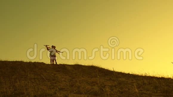 女孩在日落时玩玩具飞机孩子们手里拿着一架飞机在太阳的映衬下从山上奔跑视频的预览图