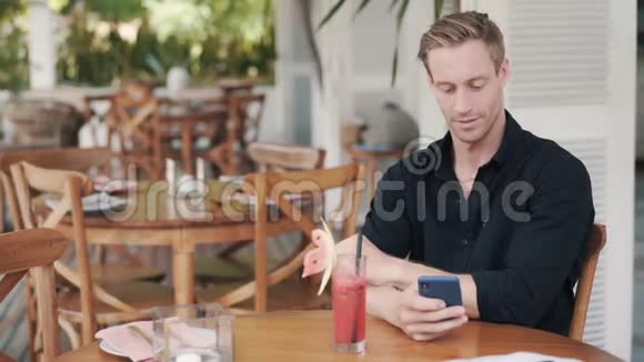 穿衬衫的帅哥坐在咖啡馆里喝果汁用电话视频的预览图