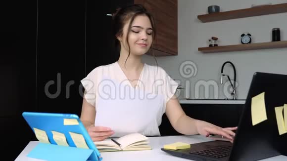 检疫期间厨房里的年轻女子女孩在笔记本电脑键盘上打字手里拿着文件呼吁视频的预览图