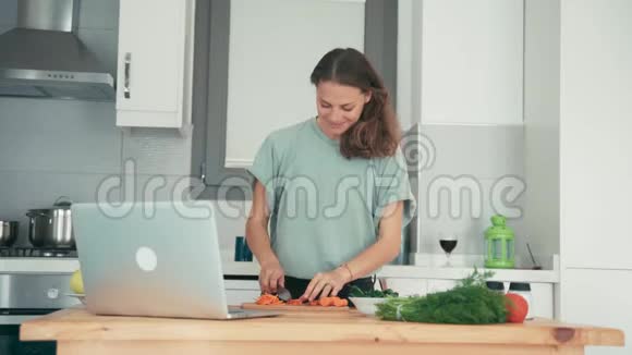 年轻女子在厨房做饭同时通过互联网与朋友交谈视频的预览图