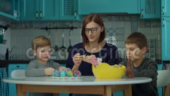 30多岁的母亲带着两个儿子在蓝色厨房的家里吃复活节巧克力兔子快乐的家庭庆祝复活节视频的预览图