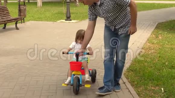快乐爸爸教小女儿骑自行车爸爸和他的孩子在户外玩耍孩子学会骑自行车视频的预览图