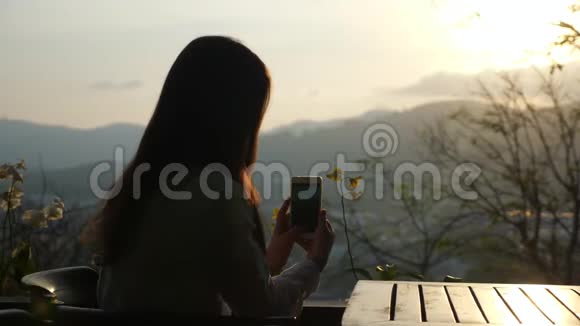 年轻女子在山上一家咖啡馆的电话里拍摄日落视频的预览图
